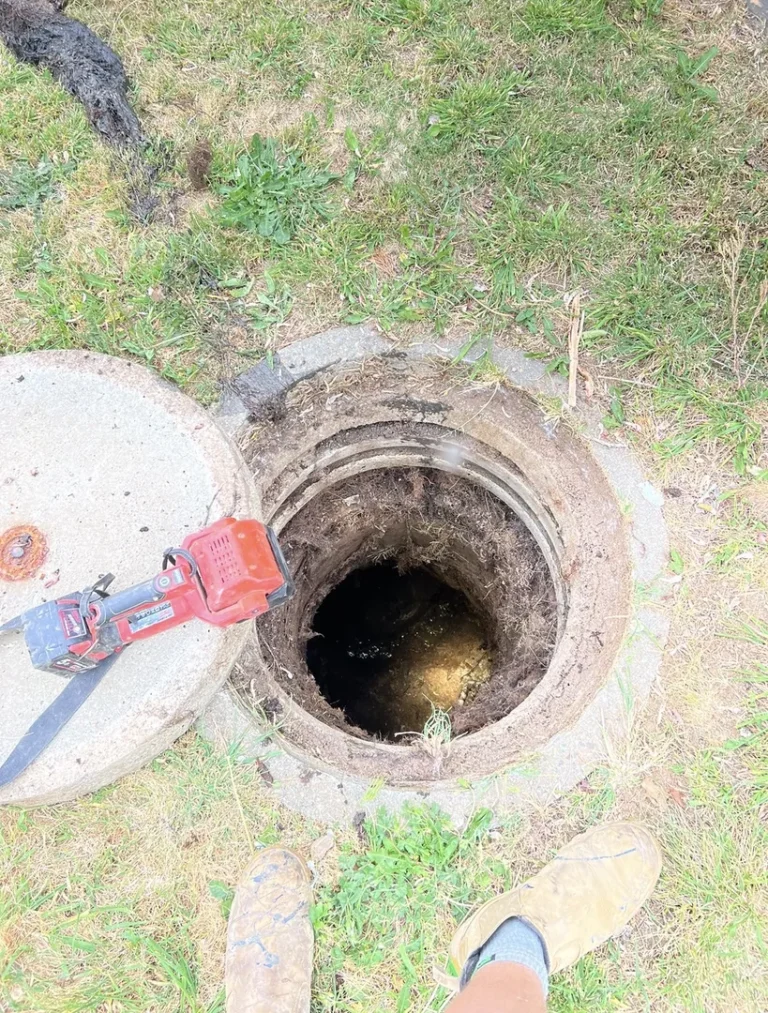 Open manhole with drill on the ground nearby.