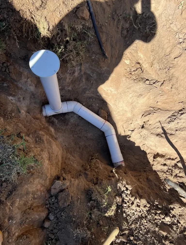 Installed vertical and horizontal PVC pipes in a dirt trench.