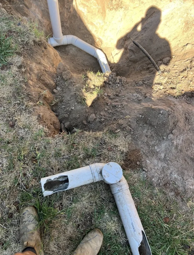 Broken PVC pipes in a trench, shadow of a person.
