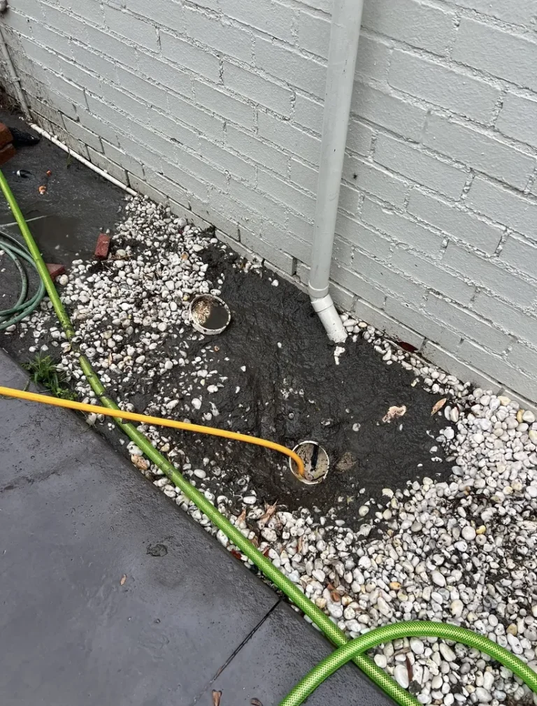 Curved drain pipe near foundation with garden hoses.